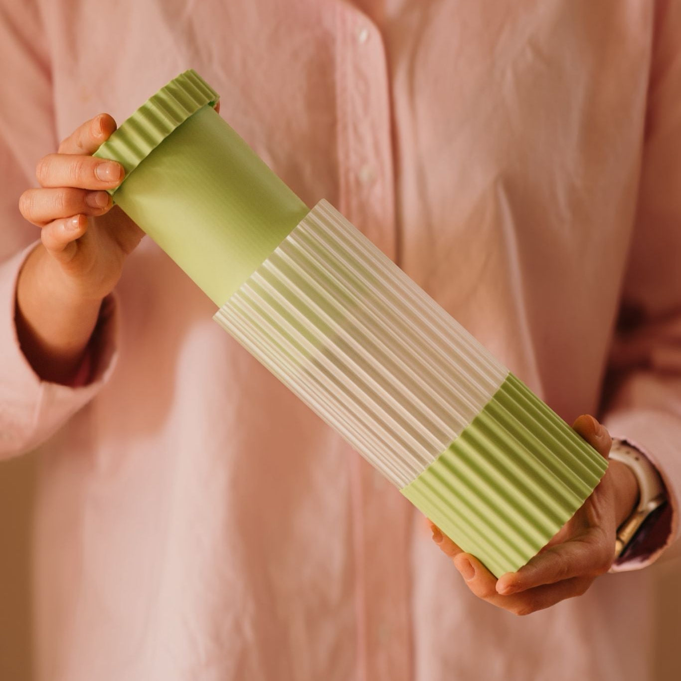 Person holding a green and clear kitchen tool against a pink background