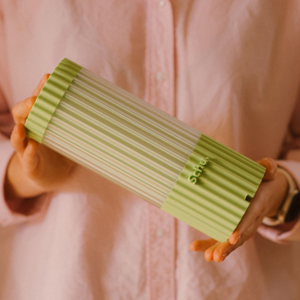 Person holding a green ribbed clutch against a pink background