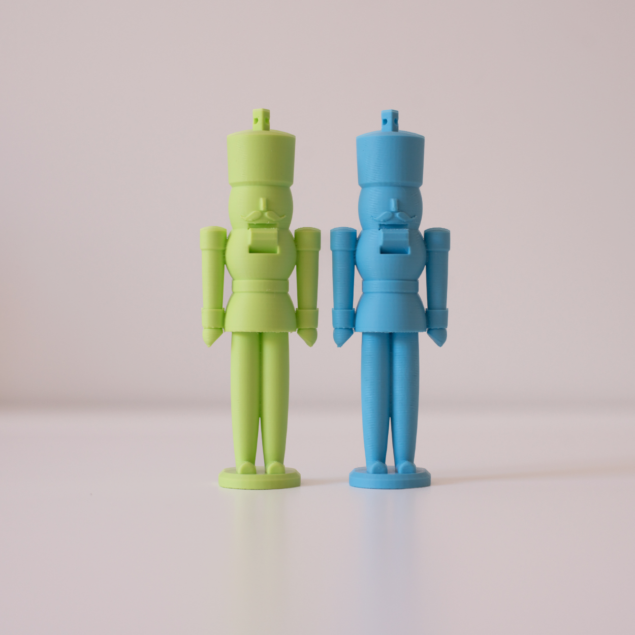 Two pastel nutcracker figures in green and blue standing side by side on a light surface with a soft background.