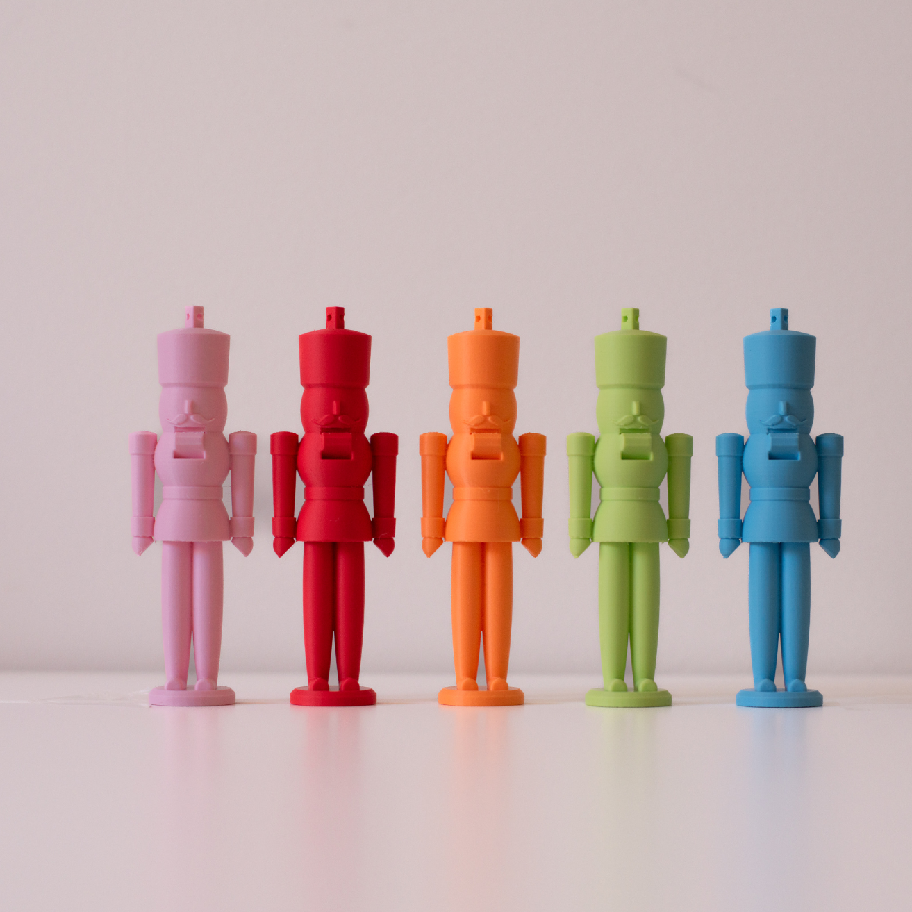 Five pastel nutcracker figures in pink, red, orange, green, and blue standing in a row on a light surface with a neutral background.